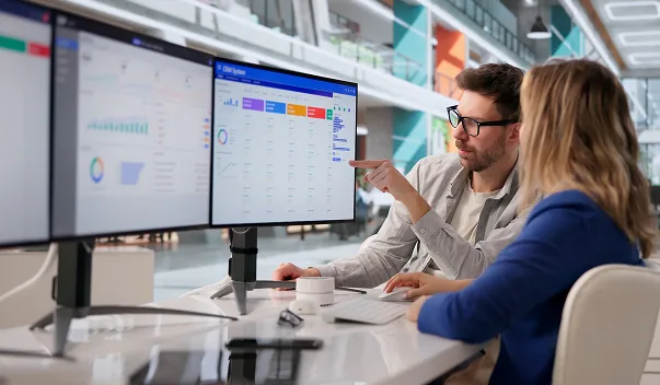 Two colleagues reviewing dashboards on a pair of monitors